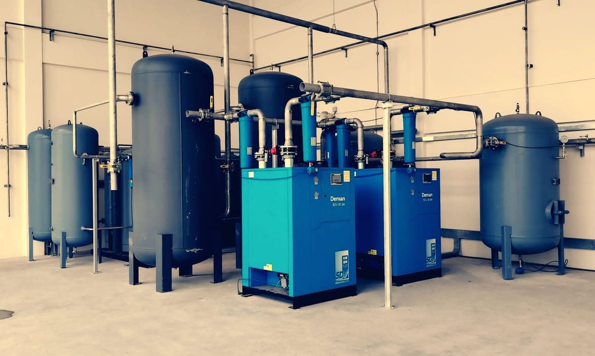 An air compressor standing on a garage floor with hose coiled beside it